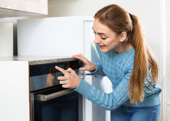 Fototapeta na wymiar Beautiful cheerful young housewife warming up electric oven