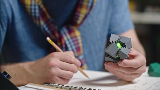 Tilt up of bearded engineer turning 3d plastic puzzle game and writing down results of test