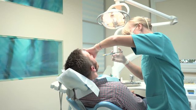 Female dentist examining an drilling patient's tooth. Visit is in proffessional dental clinic. He is sitting on dental chair. He is young and has beard. Dolly and steadicam shot.
