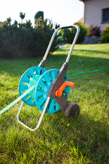 Close up detail of hose for watering the garden on the green grass (sunlight, colorful image, gardening concept, house at the background)