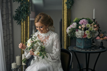 Bride smiles broad looking at a wedding bouquet while sitting in