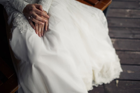 Delicate bride's hands lie on the skirt of her dress while she s
