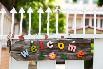 Fun colorful wooden welcome sign hanging on a white spiked fence 
