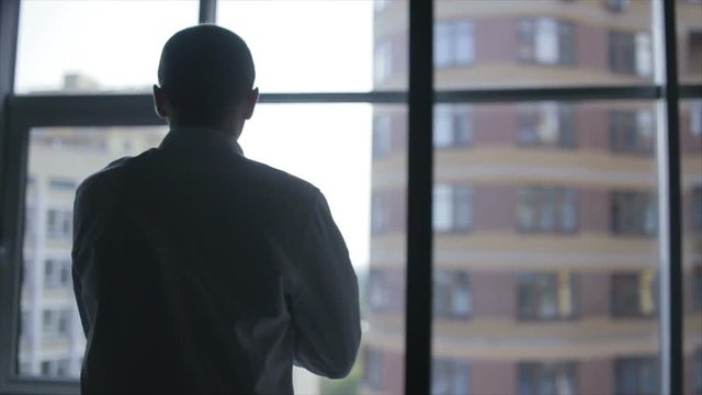Business man puts on his jacket. Businessman dressed. Silhouette of a businessman on the background of the window. Handsome man preparing for a business meeting.
