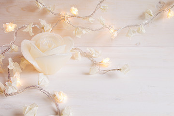 Burning lights and candle rose on white wooden background. Christmas background.