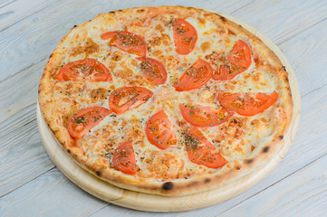 Hot vegeterian pizza with tomato, cheese and oregano on blue wooden background