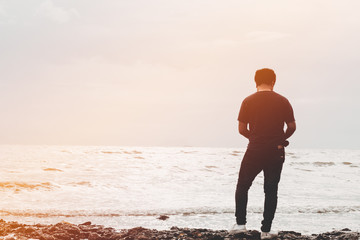 Male standing on the beach holding camera and looking to the sea.