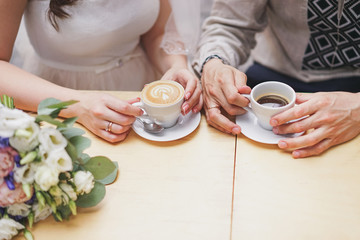 hands of the groom and the bride and coffee cups on the table