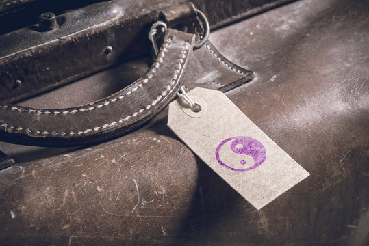Name tag with yin yang symbol on old vintage suitcase. Concept of travel with luggage, tourism and holiday destination.