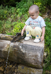 Cute kid drinking water in mountain spring