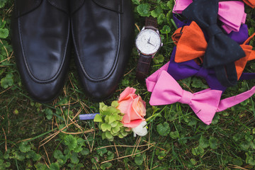 set of groom watch, boutonniere, shoes and groom's and groomsmen bow ties lie on the grass