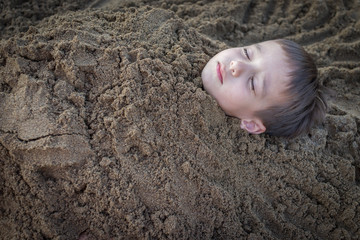 Cute kid burried in the sand for fun