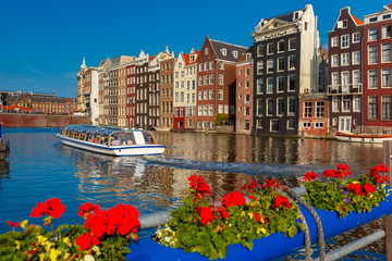 Beautiful typical Dutch dancing houses and tourist boats at the Amsterdam canal Damrak in sunny day, Holland, Netherlands.