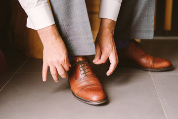 close-up of a caucasian man tie the shoelaces of his brown leather shoes