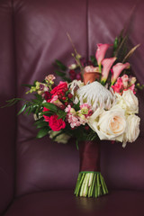 wedding bouquet of roses, berries and lilies with protea flower on purple leather background