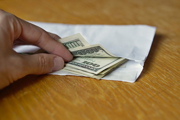 Male hand opening a white envelope full of American Dollars (USD, US Dollars) on the wooden table as a symbol of cash transfer, money laundering or bribery 