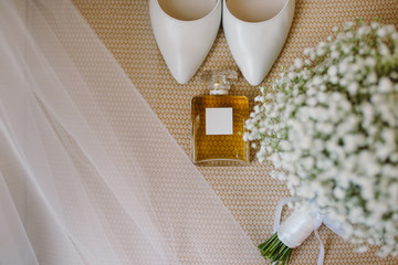 wedding set of bridal bouquet, white shoes, perfume and veil on the beige armchair