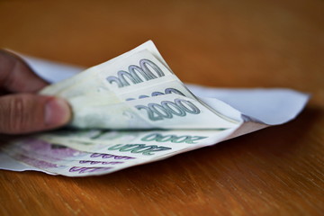Male hand opening a white envelope full of Czech currency (Czech Crowns, CZK, Kc) on the wooden table as a symbol of cash transfer, money laundering or bribery 