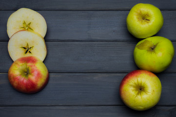 Whole and cut red and green ripe apples autumn harvest and apple juice, from above on dark grey wooden table