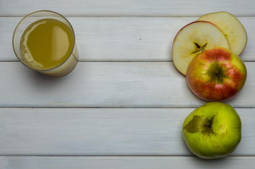 Whole and cut red and green ripe apples autumn harvest and apple juice, from above on white wooden table