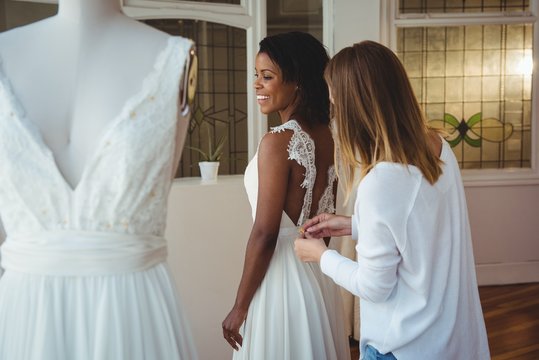 Woman trying on wedding dress with the assistance of fashion des