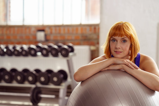 entspannte frau im fitness-studio stützt sich auf einen gymnastikball