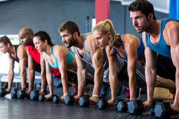 People doing push-ups with dumbbell in gym