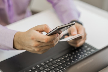 Rear view of male hands holding credit card typing numbers on smart phone