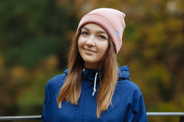 Stylish sporty brunette woman close up in trendy urban outwear posing at bridge forest city park on cold rainy fall day. Vintage filter film saturated color. Cozy bright fall season.