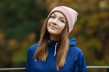 Stylish sporty brunette woman close up in trendy urban outwear posing at bridge forest city park on cold rainy fall day. Vintage filter film saturated color. Cozy bright fall season.