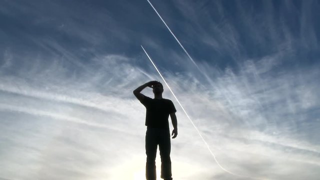 Model released man silhouette standing and saluting in front of blue sky with jet contrails.