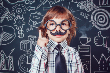 Little boy as businessman or teacher with mustache and glasses standing on dark background pattern. Wearing shirt, tie. Lifting a finger up