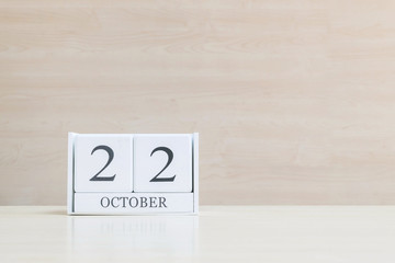 Closeup surface white wooden calendar with black 22 october word on blurred brown wood desk and wood wall textured background with copy space , selective focus at the calendar