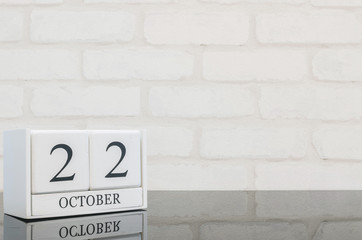 Closeup white wooden calendar with black 22 october word on black glass table and white brick wall textured background with copy space , selective focus at the calendar