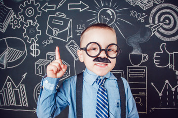 Little boy as businessman or teacher with mustache and glasses standing on dark background pattern. Wearing shirt, tie. Lifting a finger up