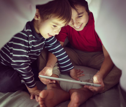 Brothers Kids With Tablet Computer Under Blanket At Night In A D