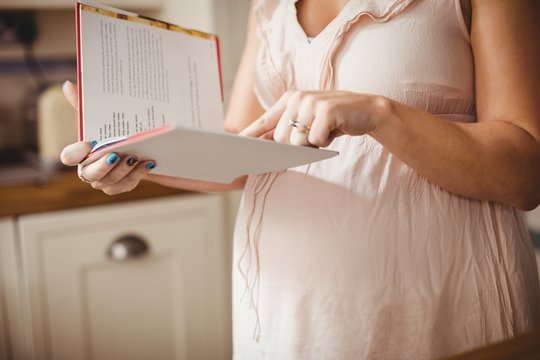 Pregnant woman reading book in kitchen