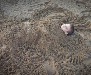 Cute kid burried in the sand for fun