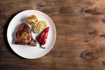 Grilled steak on brown wooden background with vegetables