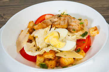 Caesar salad with croutons, cheese, eggs, tomatoes and grilled chicken on wooden table