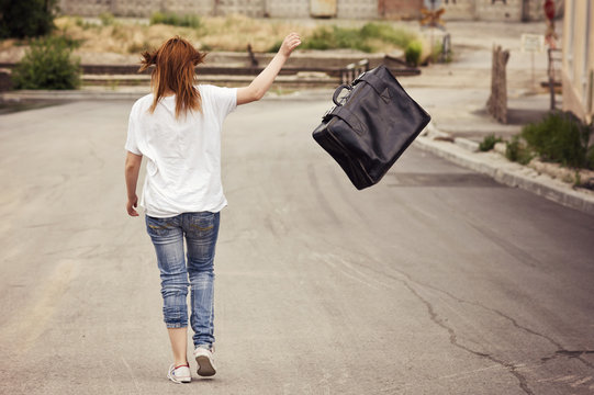 Young girl throws her suitcase walking down the street