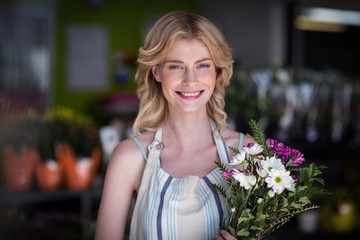 Happy female florist holding bunch of flowers in flower shop