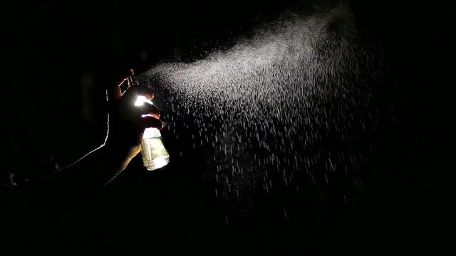 Beautiful woman's hand sprays perfume In the air. Black background.