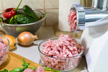 Home electric meat-grinder is making pork stuffing in a modern kitchen. Pork stuffing in a glass bowl.