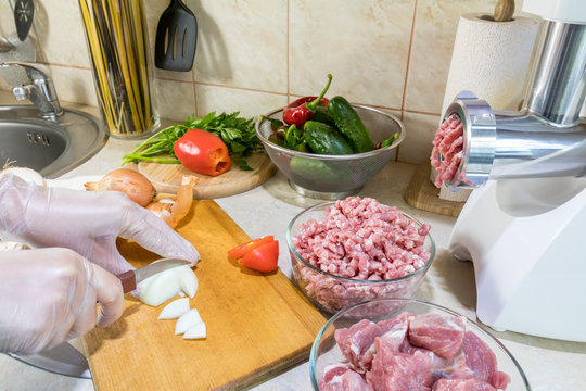 Woman is chopping onions on a wooden cutting board in the modern kitchen surrounded by fresh products, fresh vegetables and pork
