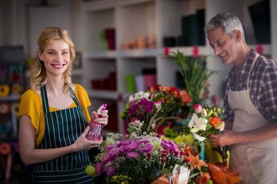 Smiling florist spraying water on flowers in flower shop