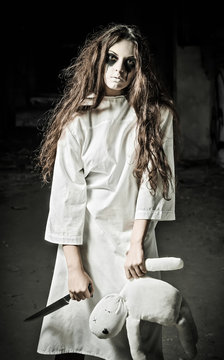 Horror style shot: strange sad girl with moppet doll and knife in hands