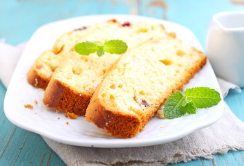 a piece of cake with raisins and candied fruit on a white plate on a blue background