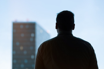 silhouette of an attractive young businessman looking at a skyscraper, graded with a lens flare

