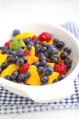 fresh berries in a white plate on a white background: raspberries, blueberries, peach.